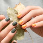 Hands with green and yellow autumn nail colours holding dry leaves