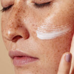 Woman applying moisturizer to freckled facial skin