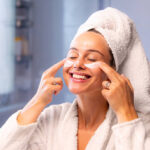 Woman applying face cream in front of a bathroom mirror